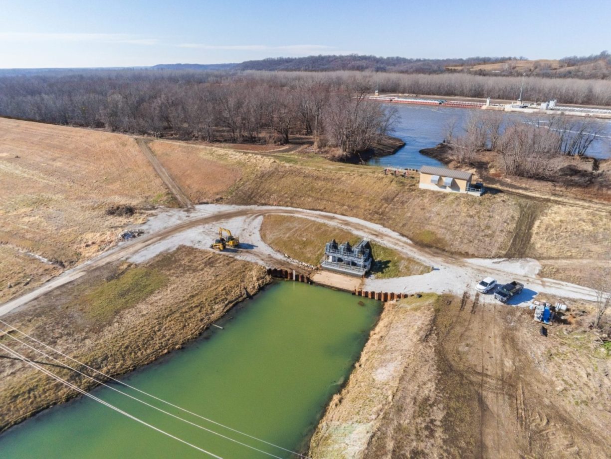 Angled aerial view with the pump station in the foreground and the Illinois river with a barge in the background