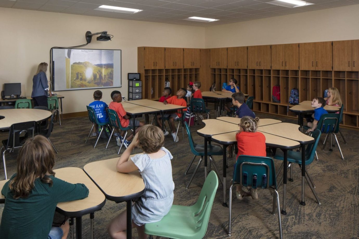 A dim lit classroom wit students looking at a projected image shown by the teacher