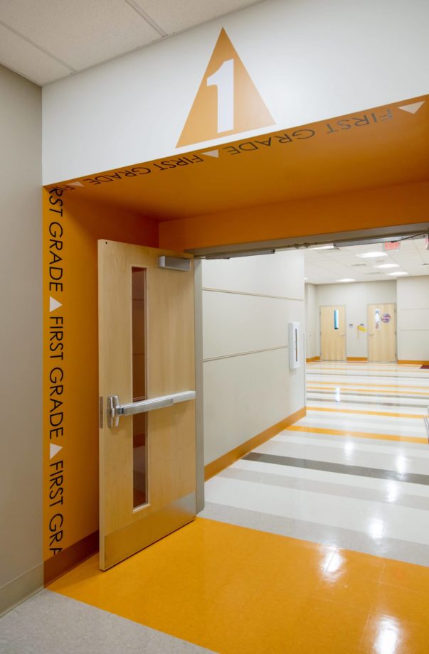 Entry into first grade pod of classrooms. The wide doorway wrapped in an orange color and an orange triangle with the number 1 is above the doorway