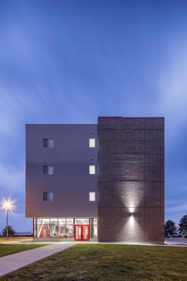 Exterior view of the SCC dorm building at dusk featuring architectural lighting with view into student lounge