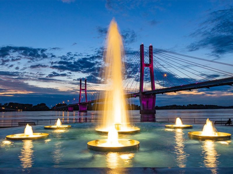 A lighted fountain in front of a lit bridge