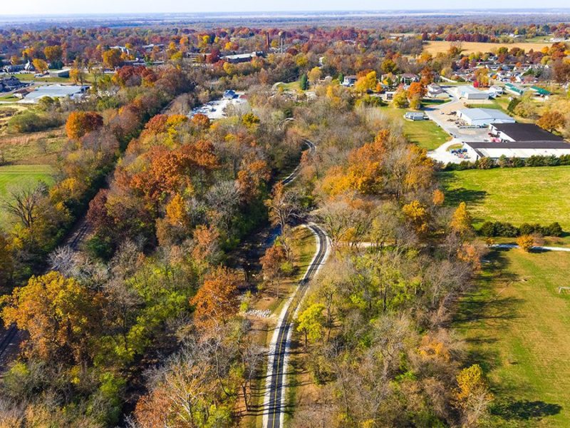 A trail running into a wooded corridor with a city on the horizon