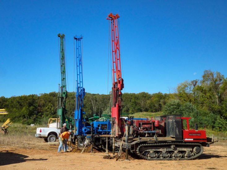 Three drill rigs sitting next to one another with two men working on them