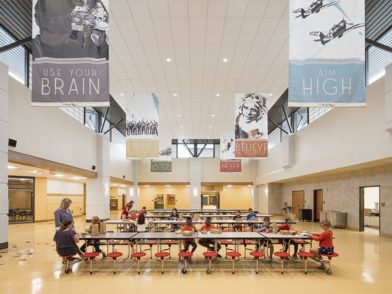 Students sitting in a school cafeteria with banners hanging from the ceiling