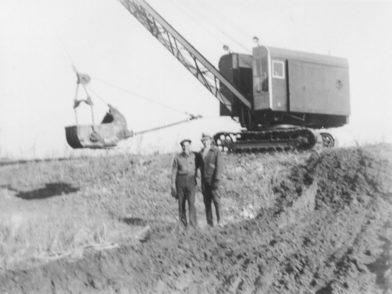 Two men standing in front of construction equipment in 1936