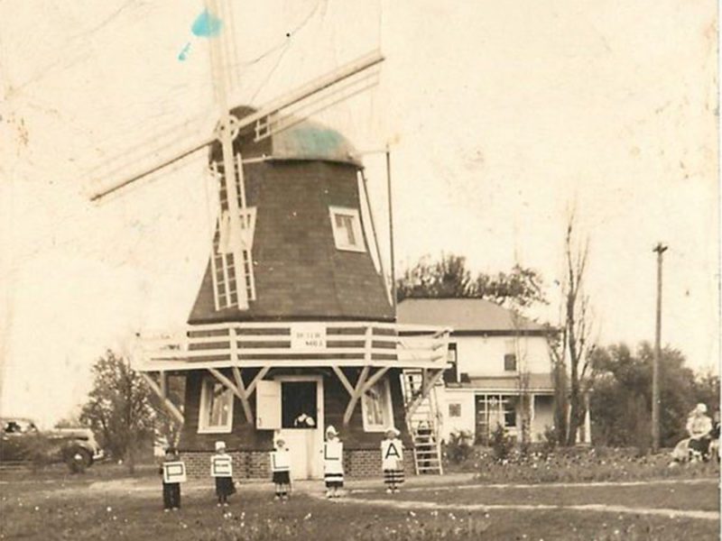 Photo of the windmill from 1930 with people holding letters that say PELLA in front of it