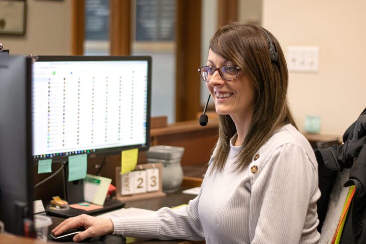 A woman sitting at a desk smiling at her computer