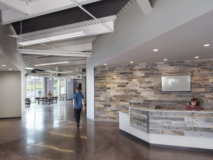 The lobby of a building with a high, open ceiling and wood panel reception desk