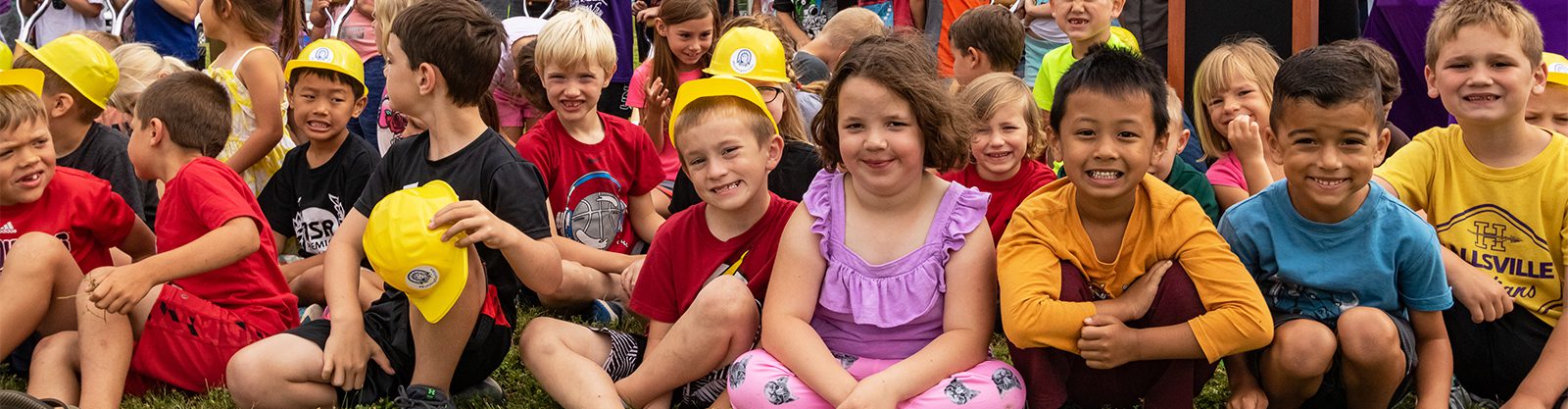 Children sitting at a groundbreaking, smiling at the camera