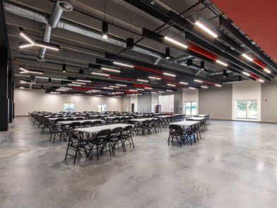 A large, open room with concrete floors and red and black baffles with tables arranged for an event